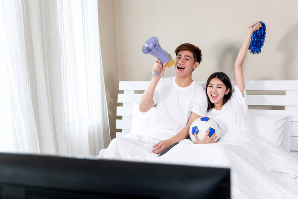 Nuori aasialainen komea aviomies ja kaunis vaimo tuntuu hyvältä, kun jalkapallo he hurraavat on voittaja mestari makuuhuoneessa - Valokuva, kuva