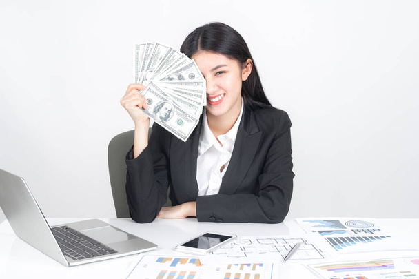Successful beautiful Asian business young woman holding money US dollar bills in hand on office desk, business concept - Fotó, kép