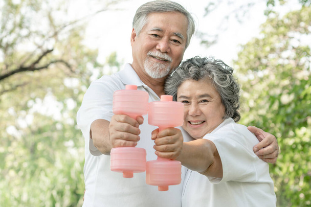 Cheerful elderly Asian man and senior Asian woman with dumbbell for workout in park, They smiling with good healthy together - Photo, Image