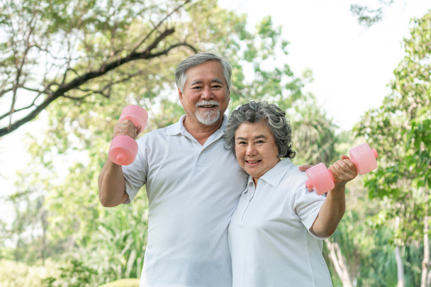 Vidám idős férfi és idős nő súlyzóval edzés a parkban, mosolyognak a jó egészséges együtt - Fotó, kép