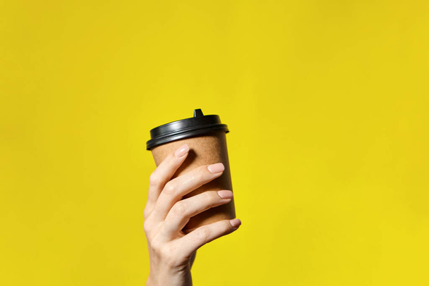 Hands holding two cups brown paper with black lid. Two coffee special offer or promo. Hands holding two cups on yellow screen background. Tea or Coffee to go. Brown paper cup with black lid. - Photo, Image