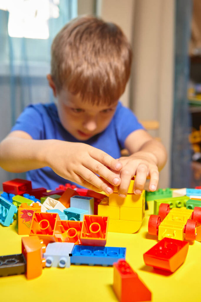 A beautiful boy is playing at home with building blocks. A cute smiling boy is playing with a lego constructor with a lot of colorful plastic blocks in the room, building a city. Preschool classes. - Photo, Image