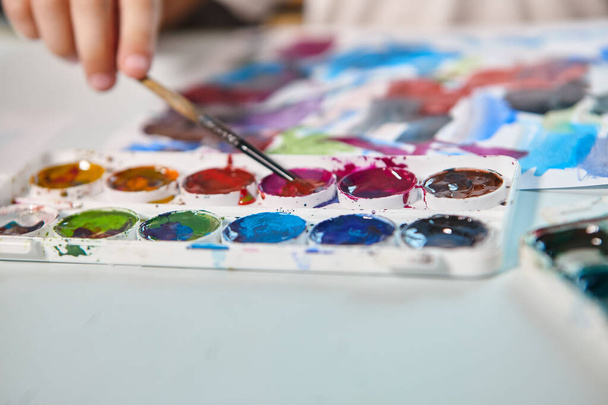 Ένα αγόρι ζωγραφίζει με μπογιές σε ένα τραπέζι στο δωμάτιό του. Υψηλής ποιότητας fullHD footageΈνα αγόρι ζωγραφίζει με χρώματα σε ένα τραπέζι στο δωμάτιό του. - Φωτογραφία, εικόνα