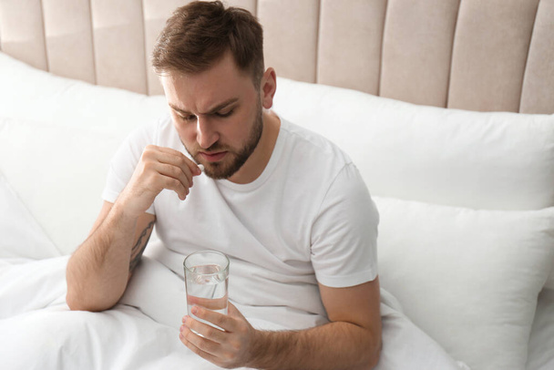Man taking pill against migraine in bed - Фото, зображення