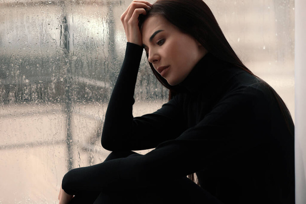 Depressed woman near window on rainy day - Foto, Imagen
