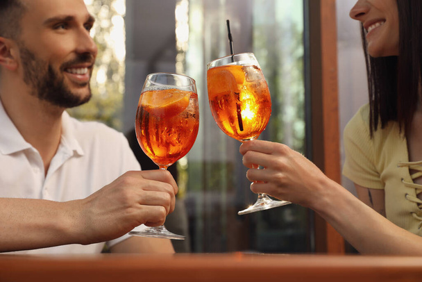 Couple clinking glasses of Aperol spritz cocktails outdoors, closeup - Фото, зображення