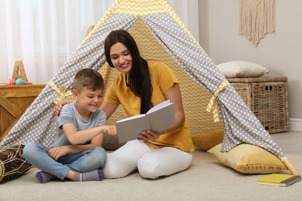 Mother and son reading book near toy wigwam at home - Photo, Image