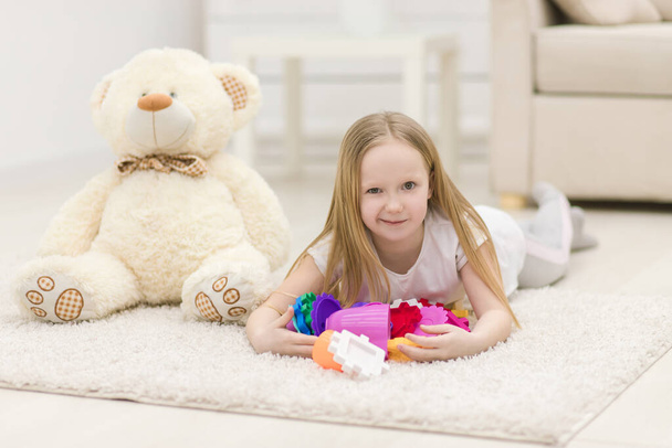 Photo of blond girl looking at the camera laying on the floor with toys. - Фото, изображение