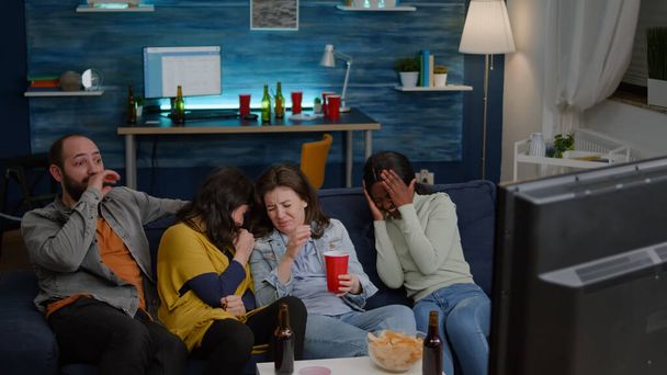 Groupe de personnes multiraciales assis confortablement sur le canapé tout en regardant film thriller - Photo, image