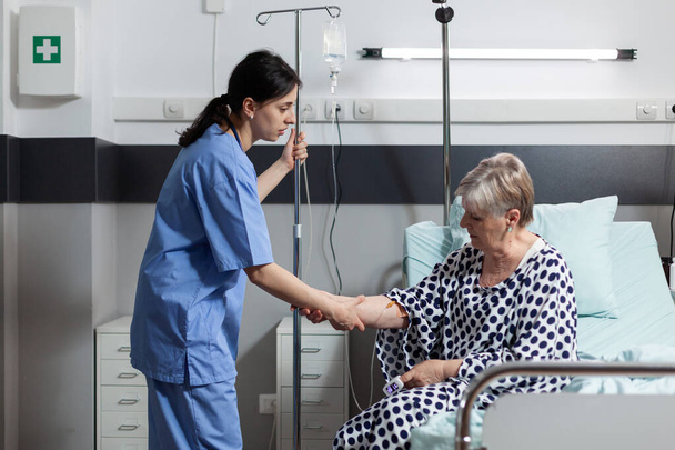 Medische verpleegkundige helpen senior vrouw patiënt opstaan uit bed - Foto, afbeelding