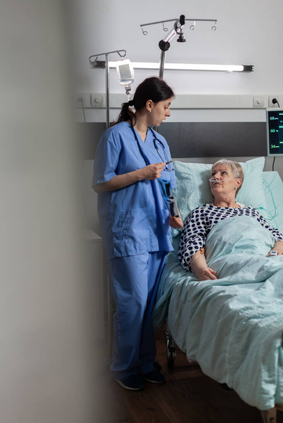 Медсестра обсуждает с пожилым пациентом во время визита рентген грудной клетки - Фото, изображение