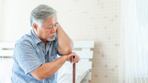 Homme âgé avec bâton de marche assis sur le lit souffrant de dépression - vieil homme souffrent de se sentir blessé et problème solitaire - Photo, image