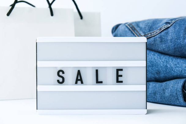 Light board with text SALE with paper shopping bags, jeans clothes. Big Sale online shopping concept. Promotion advertising. Holiday Cyber monday. - Photo, Image