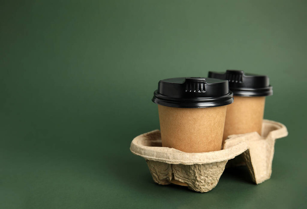 Takeaway paper coffee cups with plastic lids in cardboard holder on dark green background, space for text - Φωτογραφία, εικόνα