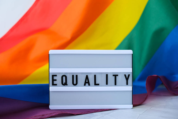 Rainbow flag with lightbox and text EQUALITY. Rainbow lgbtq flag made from silk material. Symbol of LGBTQ pride month. Equal rights. Peace and freedom. Support LGBTQ community - Photo, Image