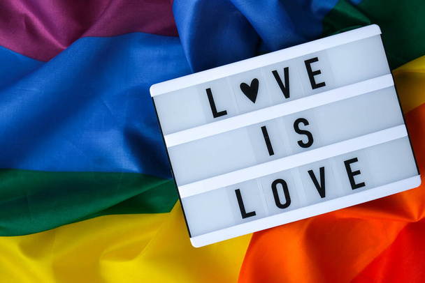 Duhová vlajka se světelnou skříňkou a textem LOVE IS LOVE. Duhová vlajka Igbtq vyrobená z hedvábného materiálu. Symbol měsíce pýchy LGBTQ. Rovná práva. Mír a svoboda. Podpora komunity LGBTQ - Fotografie, Obrázek