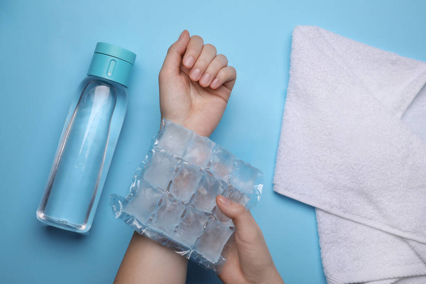 Woman with ice pack, bottle of water and towel on light blue background, top view. Heat stroke treatment - Foto, imagen
