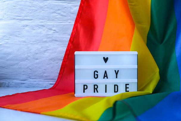 Regenboogvlag met lichtbak en tekst GAY PRIDE. Rainbow lgbtq vlag gemaakt van zijde materiaal. Symbool van LGBTQ trots maand. Gelijke rechten. Vrede en vrijheid. Ondersteuning van de LGBTQ gemeenschap - Foto, afbeelding