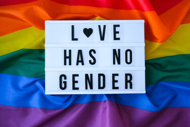 Regenboogvlag met lichtbak en tekst LIEFDE HEEFT GEEN GENDER. Rainbow lgbtq vlag gemaakt van zijde materiaal. Symbool van LGBTQ trots maand. Gelijke rechten. Vrede en vrijheid. Ondersteuning van de LGBTQ gemeenschap - Foto, afbeelding
