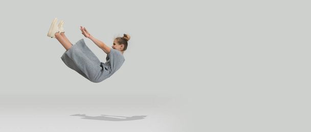Studio shot of little preschool caucasian girl in casual clothes falling down isolated over white studio background. - Фото, изображение