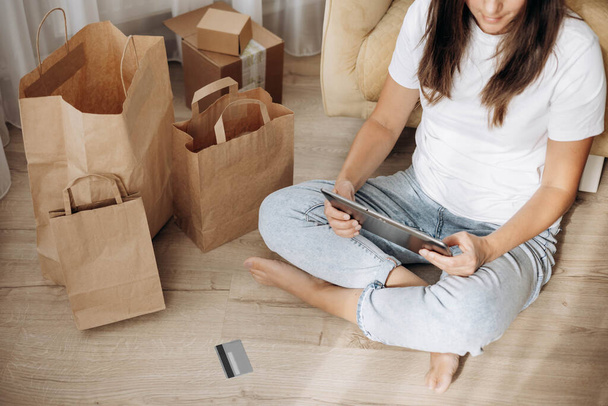 Woman sitting on floor, holding credit bank card and using tablet for online shopping at home. Selective focus - Foto, imagen