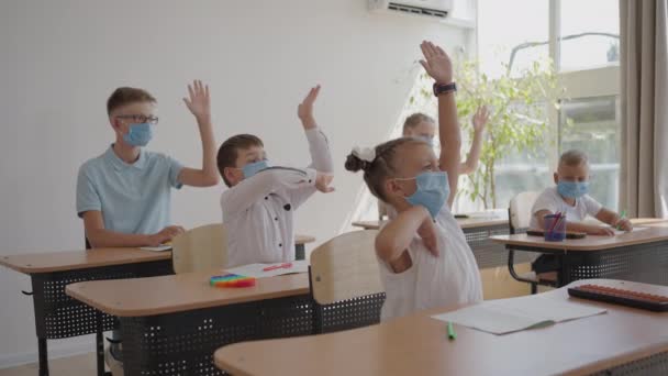 仮面の学校の教室の子供たちは教室に座ってゆっくりと手を挙げて先生の質問に答えます。学校でのパンデミック時の教訓 - 映像、動画