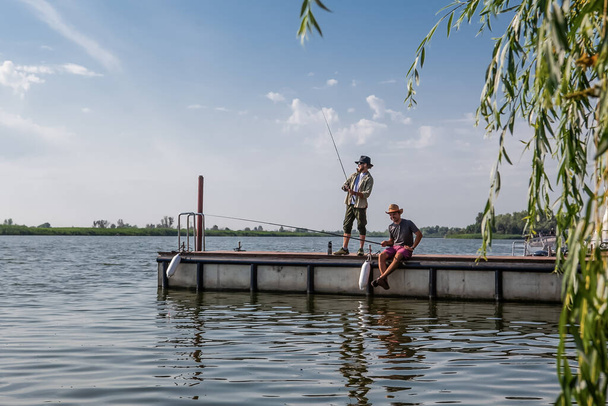 Два человека на пирсе летом ловят рыбу удочками. - Фото, изображение