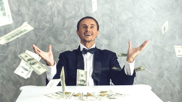 Счастливый бизнесмен очень богатый парень бросает деньги долларовые купюры в воздух, как деньги дождя законопроект и банкноты доллар США законопроект на стол - бизнес-концепции успеха - Фото, изображение