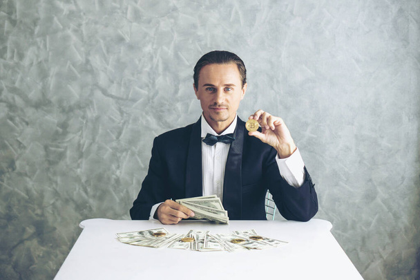 İş adamı zengini tüccar Bitcoin altın sikkesi tutuyor Bitcoin tüccarı için yeni para değişimi ve masa başı iş konsepti üzerine Amerikan doları banknotları - Fotoğraf, Görsel