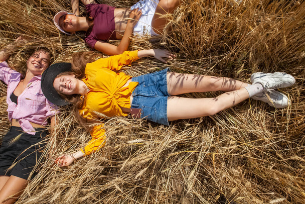 τρεις νεαρές γυναίκες ξαπλώνουν στο κίτρινο γρασίδι το καλοκαίρι - Φωτογραφία, εικόνα