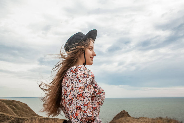 kobieta w czarnym kapeluszu na skraju kanionu z widokiem na morze w lecie - Zdjęcie, obraz