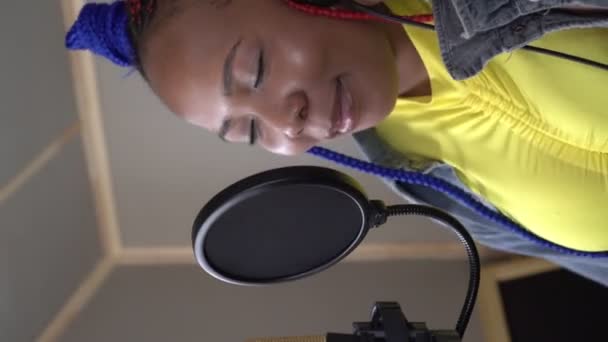 Vertical video: Młoda czarna piosenkarka nagrywa piosenkę w studiu nagraniowym - Materiał filmowy, wideo