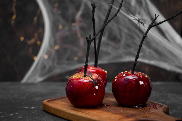  Red apples in caramel with a festive Halloween decor, an original treat for a festive Halloween table decorated with spiders and cobwebs, copy space for text - Foto, Imagen