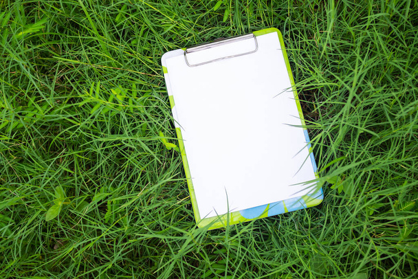 Mock up empty white paper on file document with green grass background.card on nature for message flat lay with free space for add text or products presentation. business and lifestyle environment. - Photo, image