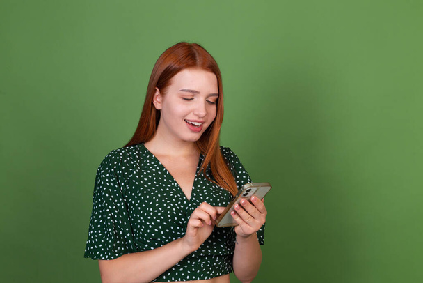Young red hair woman on green background with  mobile phone happy positive excited - 写真・画像