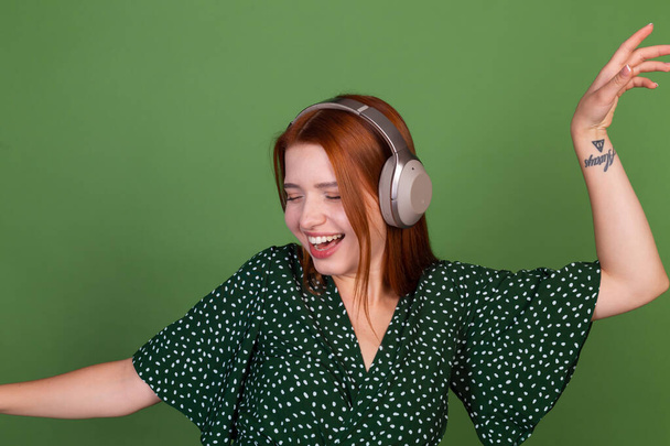 若いです赤い髪の女性緑の背景に無線ヘッドフォンと幸せな移動ダンス周り - 写真・画像