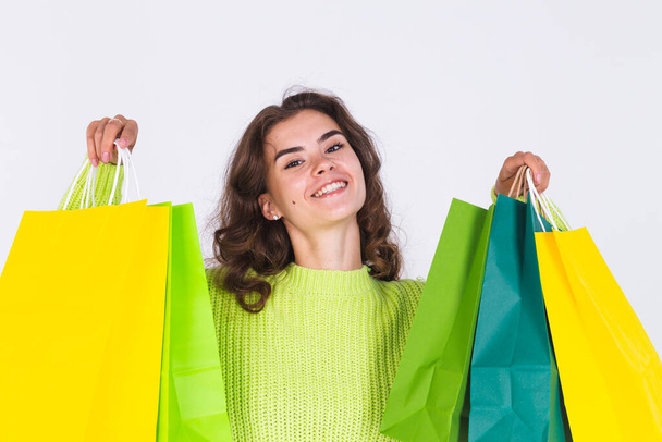 Young beautiful woman with freckles light makeup in sweater on white background with shopping bags cheerful happy excited - Photo, Image