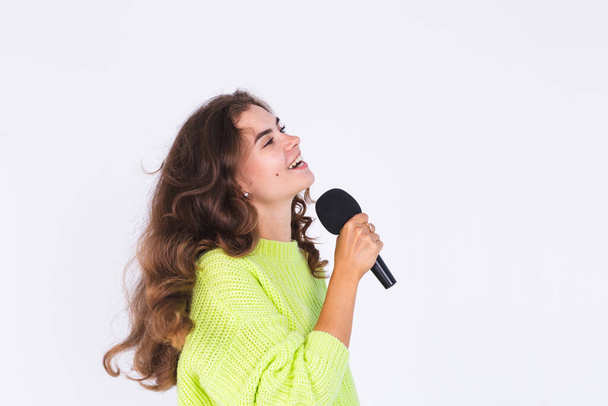 Genç, çilli, hafif makyajlı, beyaz arka planda, mikrofonlu mutlu şarkı söyleyen güzel bir kadın. - Fotoğraf, Görsel