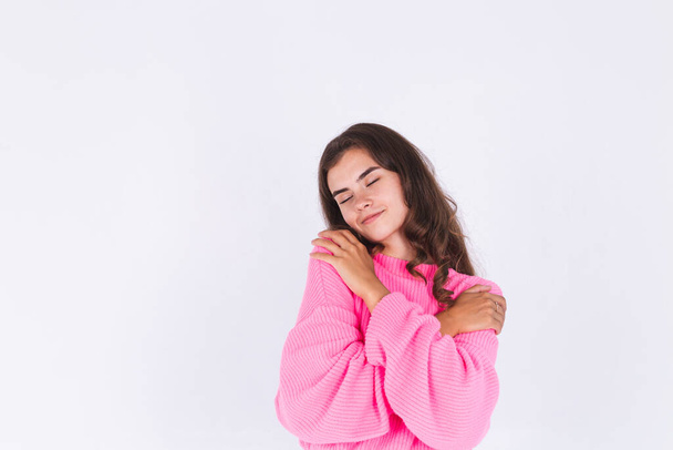 Young beautiful woman with freckles light makeup in sweater on white background hugging herself, self care  and love concept - Foto, imagen
