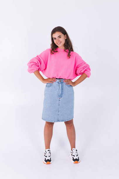 Young beautiful woman with freckles light makeup in pink sweater and jeans skirt on white background posing stylish full length - Fotó, kép