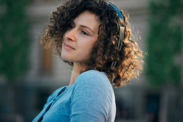 A young woman dressed trendy standing on the street and listening to music. - Foto, imagen