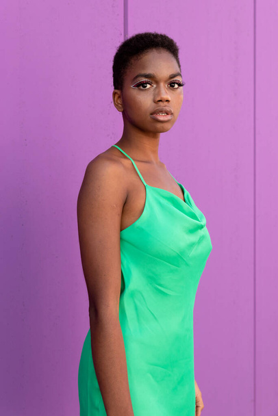 カメラを見ているライラックの背景の前に電気緑のドレスで短い髪を持つスタイリッシュな若い黒人女性 - 写真・画像