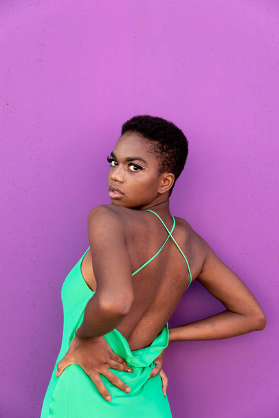 Back view of stylish young black woman with short hair in electric green dress in front of a lilac background  - Photo, Image