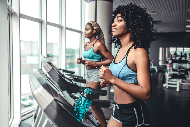 Side view of two attractive sports african women on running track. Girls on treadmill. Calories burn. - Fotoğraf, Görsel