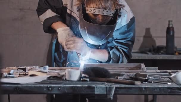 Junge Arbeiter in Schutzhandschuhen und Helm schweißen Teile des Metalldetails zusammen - Filmmaterial, Video
