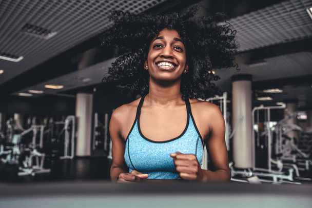 young afro woman with curly hair exercise fitness and workout while run on track in sport club. Sexy sporty girl on treadmill - Фото, изображение
