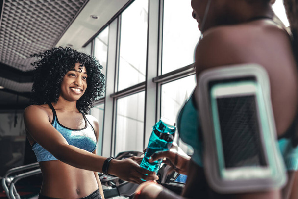 Vágott kép fekete lány ad üveg vizet a nők a tornaterem edzés után. Egészséges sportos életmód - Fotó, kép