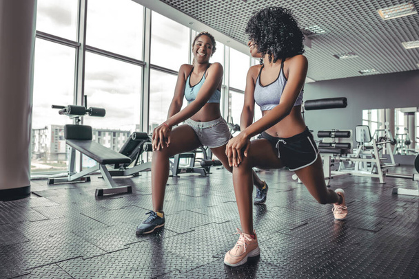 Fitness african women doing lunges exercises for leg muscle workout training in gym. Active black girls doing front forward one leg step lunge exercise. Weightloss pilates concept - Zdjęcie, obraz