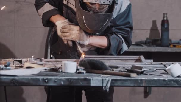 Joven trabajador en guantes de protección y piezas de soldadura casco del detalle de metal juntos - Metraje, vídeo