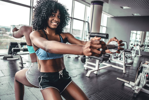 Fitness, sport, training and lifestyle concept - group of happy women with dumbbells flexing muscles in gym staying back to back - Foto, afbeelding